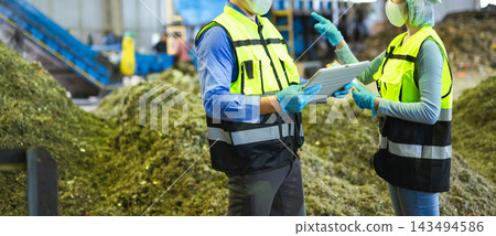 Midsection of two industrial workers in safety vests using a digital tablet to inspect organic waste processing and sorting 143494586