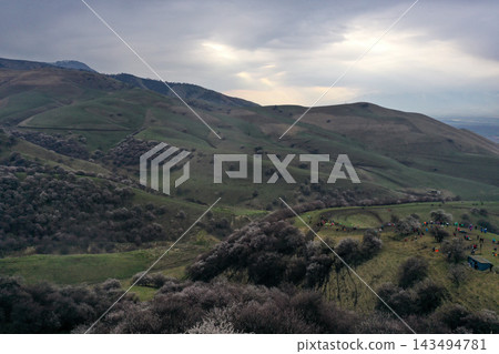 從空中俯瞰中國新疆維吾爾自治區寬闊山谷山坡上舉行的春季節日，人群熙熙攘攘。 143494781
