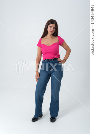Young woman standing confidently in a studio, wearing a bright pink ribbed top, blue high waisted jeans, and black shoes, presenting modern fashion and style Young woman standing confidently in a studio, wearing a bright pink ribbed top, blue high waisted jeans, and black shoes, presenting modern fashion and style 143494942