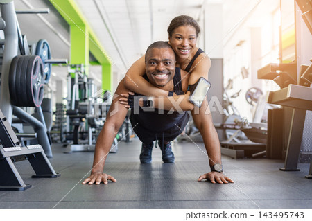 Happy black couple doing push-ups in gym, woman hugging man from behind Happy black couple doing push-ups in gym, woman hugging man from behind 143495743