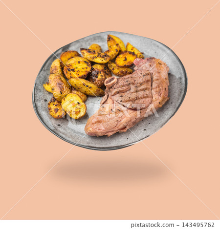 Grilled lamb chop with roasted potatoes on a gray plate floating above a soft shadow on a peach background Grilled lamb chop with roasted potatoes on a gray plate floating above a soft shadow on a peach background 143495762