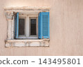 Old architectural window with weathered blue wooden shutters set in a sand-colored wall in Egypt, featuring traditional historic architecture and authentic aged details 143495801