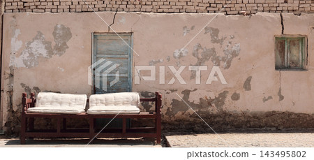 Old wooden outdoor sofa standing beside a weathered house in Egypt, featuring aged furniture, rustic character and authentic traditional architecture Old wooden outdoor sofa standing beside a weathered house in Egypt, featuring aged furniture, rustic character and authentic traditional architecture 143495802