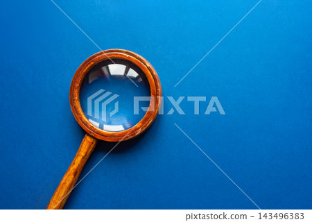Vintage wooden magnifying glass with brass ring on vibrant blue background Vintage wooden magnifying glass with brass ring on vibrant blue background 143496383