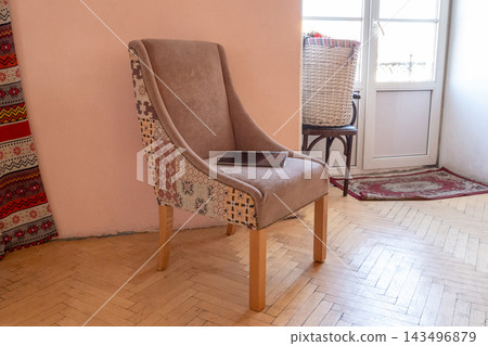 Upholstered armchair with tablet beside balcony doors. Eclectic living room with patterned textiles and woven basket. Home interior decor. Digital devices in a domestic reading space. Upholstered armchair with tablet beside balcony doors. Eclectic living room with patterned textiles and woven basket. Home interior decor. Digital devices in a domestic reading space. 143496879