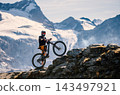 Mountain biker riding on a rocky alpine trail with snow-covered peaks and glaciers in the background, capturing outdoor adventure, mountain biking and dramatic high altitude scenery. 143497921