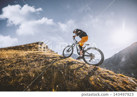 Mountain biker riding across a rugged alpine slope with dramatic mountain scenery, warm sunlight and rocky terrain, capturing outdoor adventure, mountain biking and high altitude freedom. Mountain biker riding across a rugged alpine slope with dramatic mountain scenery, warm sunlight and rocky terrain, capturing outdoor adventure, mountain biking and high altitude freedom. 143497923