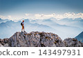 Hiker standing on a rocky summit during a via ferrata in the Austrian Alps near Innsbruck, Tyrol, with dramatic mountain peaks and a vast alpine landscape in the background. 143497931