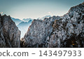 Solo male climber ascending a vertical rock wall on a via ferrata in the Austrian Alps near Innsbruck, Tyrol, with rugged cliffs and distant mountain peaks creating a dramatic alpine scene. 143497933