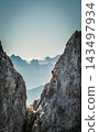 Solo male climber ascending a vertical rock wall on a via ferrata in the Austrian Alps near Innsbruck, Tyrol, with rugged cliffs and distant mountain peaks creating a dramatic alpine scene. 143497934