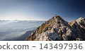 Hiker standing on a rocky summit during a via ferrata in the Austrian Alps near Innsbruck, Tyrol, with dramatic mountain peaks and a vast alpine landscape in the background. 143497936