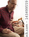 Middle-Aged Man Clutching Chest in Pain on Sofa 143499559