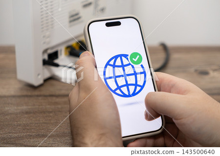 A person holds a smartphone displaying a globe icon with a checkmark to verify a successful internet router connection, symbolizing network stability and reliable high speed connectivity A person holds a smartphone displaying a globe icon with a checkmark to verify a successful internet router connection, symbolizing network stability and reliable high speed connectivity 143500640