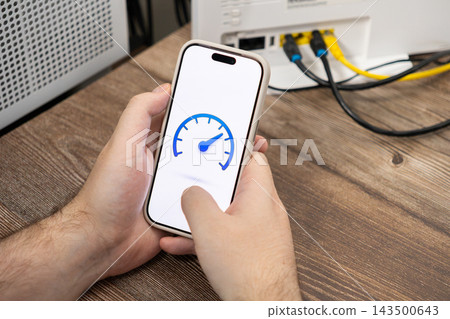 Person holding a smartphone displaying a speed test gauge icon near a home router to assess fast wireless internet performance and network connectivity for reliable remote digital work 143500643
