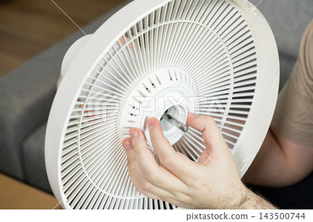 A technician mounts a plastic fan guard onto a metal spindle, ensuring the cooling device is properly assembled during home maintenance to restore airflow for improved room comfort A technician mounts a plastic fan guard onto a metal spindle, ensuring the cooling device is properly assembled during home maintenance to restore airflow for improved room comfort 143500744