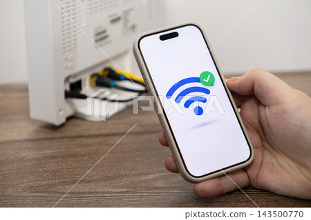 A person holds a smartphone displaying a successful wireless connection icon near a home router, illustrating high speed internet access setup and reliable digital network connectivity A person holds a smartphone displaying a successful wireless connection icon near a home router, illustrating high speed internet access setup and reliable digital network connectivity 143500770