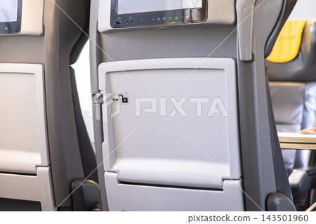 Closed tray table on an airplane seat with an unlocking icon, representing travel preparation and flight safety protocols for passengers during commercial air transportation services Closed tray table on an airplane seat with an unlocking icon, representing travel preparation and flight safety protocols for passengers during commercial air transportation services 143501960