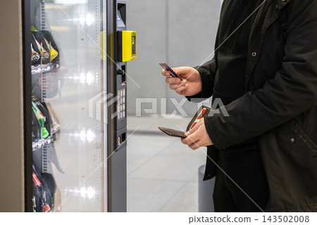 A man holds a credit card to pay for a snack at a vending machine in a modern public terminal, highlighting convenient cashless purchase options for commuters in a busy urban area A man holds a credit card to pay for a snack at a vending machine in a modern public terminal, highlighting convenient cashless purchase options for commuters in a busy urban area 143502008