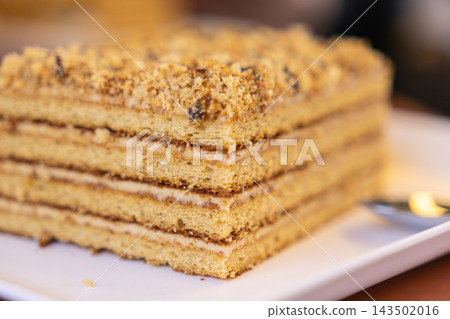 Layered honey cake slice on a white plate, featuring thin sponge sections with creamy frosting and crumb topping for a delicious dessert experience in a cafe or home kitchen setting Layered honey cake slice on a white plate, featuring thin sponge sections with creamy frosting and crumb topping for a delicious dessert experience in a cafe or home kitchen setting 143502016