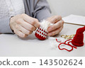 Hands of a person sewing together knitted parts of a Tomte doll made from yarn. 143502624