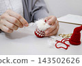 Hands of a person sewing together knitted parts of a Tomte doll made from yarn. 143502626