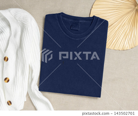 Washed navy blue folded t-shirt mockup near cardigan and palm leaf, template for print on demand Washed navy blue folded t-shirt mockup near cardigan and palm leaf, template for print on demand 143502701