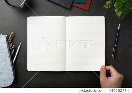 Top view of opened black hardcover notebook with hand hold page and office stationery on dark stone background with copy space Top view of opened black hardcover notebook with hand hold page and office stationery on dark stone background with copy space 143502784