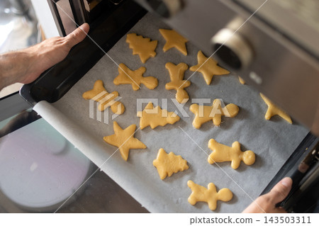 Placing tray of homemade Christmas cookies into oven Placing tray of homemade Christmas cookies into oven 143503311