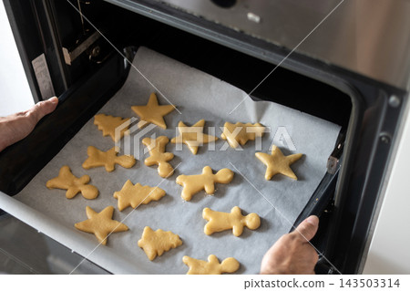 Placing tray of homemade Christmas cookies into oven Placing tray of homemade Christmas cookies into oven 143503314