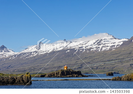Orange lighthouse on rocky islet below snowy mountains in East Iceland Orange lighthouse on rocky islet below snowy mountains in East Iceland 143503398