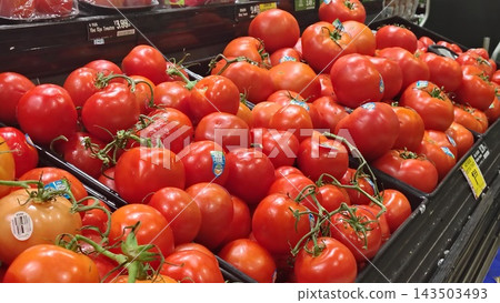 ripe red tomatoes on the vine on a supermarket display. A neat arrangement of juicy tomatoes with price tags in the store's produce section. 143503493