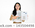 Young Asian Woman Smiling and Pointing at a Large Calculator on White Background 143504498
