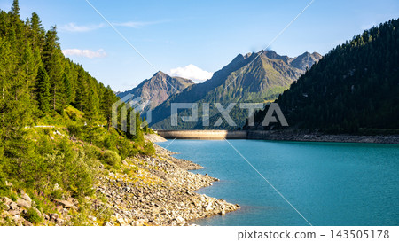 Lake Neves sits at the end of the Molini Valley in the Zillertal Alps, Italy. It features clear blue water and surrounding mountains with green trees. People may walk along the shore. Lake Neves sits at the end of the Molini Valley in the Zillertal Alps, Italy. It features clear blue water and surrounding mountains with green trees. People may walk along the shore. 143505178