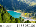Lake Neves is in South Tyrol at the end of the Molini Valley in the Zillertal Alps. This view shows the clear water and surrounding green trees on a sunny day. 143505180