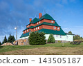 This is Masaryk's cottage located on Serlich. It is a well-known mountain cottage in the Orlicke ountains. The structure features multiple roofs and is surrounded by grass and trees. 143505187