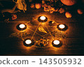Authentic pagan altar with drawn pentagram circle and burning candles, a bird skull, autumn flowers, crystals and apples on wooden surface in the dark. 143505932