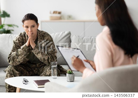 Worried Woman In Military Uniform, Engaged In Therapy Session With Female Therapist At Office, Seeking Mental Health Support And Guidance In Professional Healthcare Environment. Worried Woman In Military Uniform, Engaged In Therapy Session With Female Therapist At Office, Seeking Mental Health Support And Guidance In Professional Healthcare Environment. 143506337