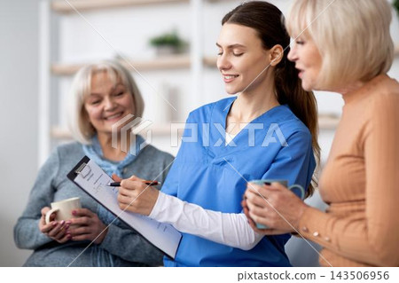 Smiling Female Nurse Engaging With Senior Caucasian Women During Consultation In Modern Healthcare Clinic. Providing Support And Guidance In Comfortable Setting. Healthcare Concept. Smiling Female Nurse Engaging With Senior Caucasian Women During Consultation In Modern Healthcare Clinic. Providing Support And Guidance In Comfortable Setting. Healthcare Concept. 143506956