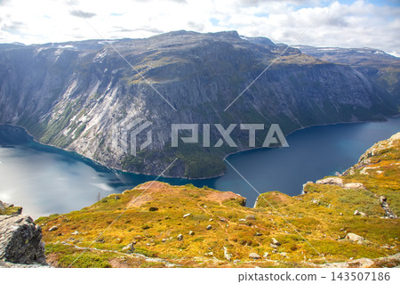 View of a fjord in Norway surrounded by cliffs and hills during a clear day View of a fjord in Norway surrounded by cliffs and hills during a clear day 143507186
