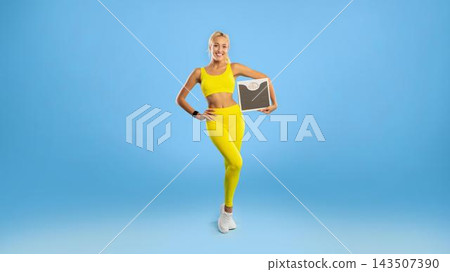Smiling Young Woman In Yellow Activewear Holding A Weight Scale At Gym, Showcasing A Positive Emotion. Engaging In Fitness Routine In A Bright Studio Setting. Weight Loss Concept. Smiling Young Woman In Yellow Activewear Holding A Weight Scale At Gym, Showcasing A Positive Emotion. Engaging In Fitness Routine In A Bright Studio Setting. Weight Loss Concept. 143507390