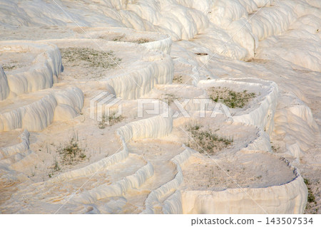 White travertine terraces in Pamukkale, Turkey with small patches of greenery on the slopes 143507534