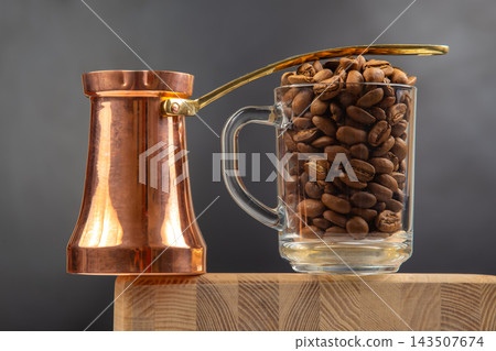 Coffee beans in glass mug next to traditional copper coffee pot on wooden surface Coffee beans in glass mug next to traditional copper coffee pot on wooden surface 143507674