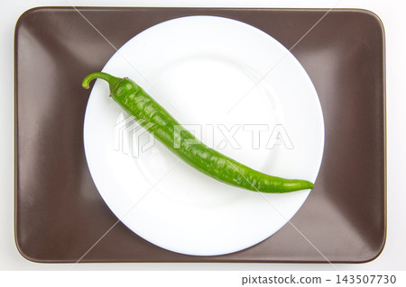 Green chili pepper on a white plate placed on a brown tray in a well-lit setting Green chili pepper on a white plate placed on a brown tray in a well-lit setting 143507730