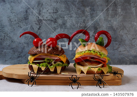 Scary hamburgers with fresh lettuce, tomatoes, cream cheese, lettuce, onions, cutlets and peppers in the form of horns on an old concrete background, cafe advertising, menu, restaurant business card, Scary hamburgers with fresh lettuce, tomatoes, cream cheese, lettuce, onions, cutlets and peppers in the form of horns on an old concrete background, cafe advertising, menu, restaurant business card, 143507976