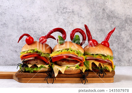 Halloween food concept. Scary hamburgers with fresh lettuce, tomatoes, cream cheese, lettuce, onions, cutlets and peppers in the form of horns on an old concrete background, cafe advertising, menu, Halloween food concept. Scary hamburgers with fresh lettuce, tomatoes, cream cheese, lettuce, onions, cutlets and peppers in the form of horns on an old concrete background, cafe advertising, menu, 143507978