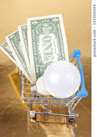 Shopping cart with light bulb and one dollar bills on golden background 143508484