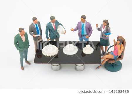 Miniature people gather around a table to discuss gear models in a meeting setting 143508486
