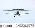 Small plane flies in the sky during daytime near a rural area with fields and trees 143508575