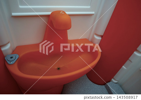 Orange plastic hand washing sink inside a portable public toilet cabin Orange plastic hand washing sink inside a portable public toilet cabin 143508917