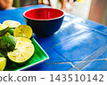 Sliced limes and whole limes on a green plate placed on a bright blue plastic table. 143510142
